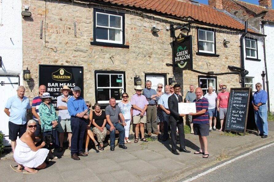 Group of people standing in front of pub holing a giant cheque