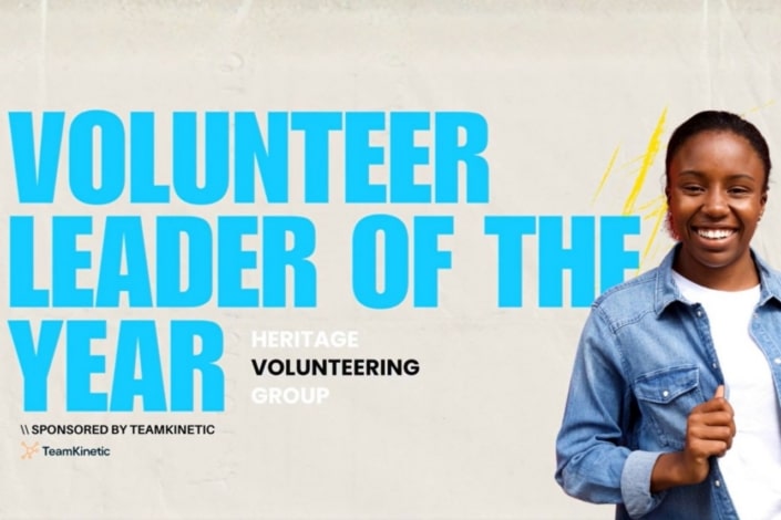 A smiling young woman in a denim shirt stands beside large blue text reading Volunteer Leader of the Year, celebrating her recognition with the prestigious Volunteer Award. Smaller text highlights Heritage Volunteering Group and Sponsored by TeamKinetic.