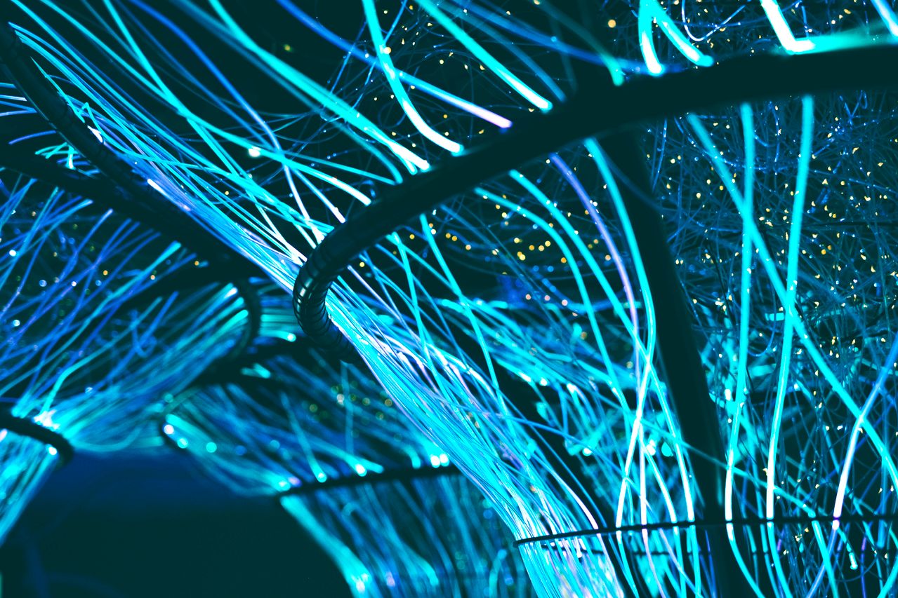 Curved structures with glowing blue and teal fibre optic cables intertwining, creating a futuristic, neural network-like appearance on a dark background.