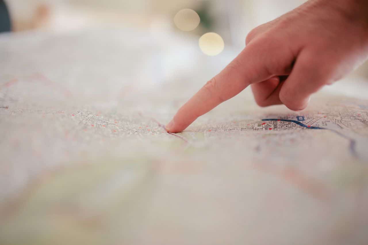 A close-up of a hand pointing at a specific location on a paper map, with the background softly blurred.