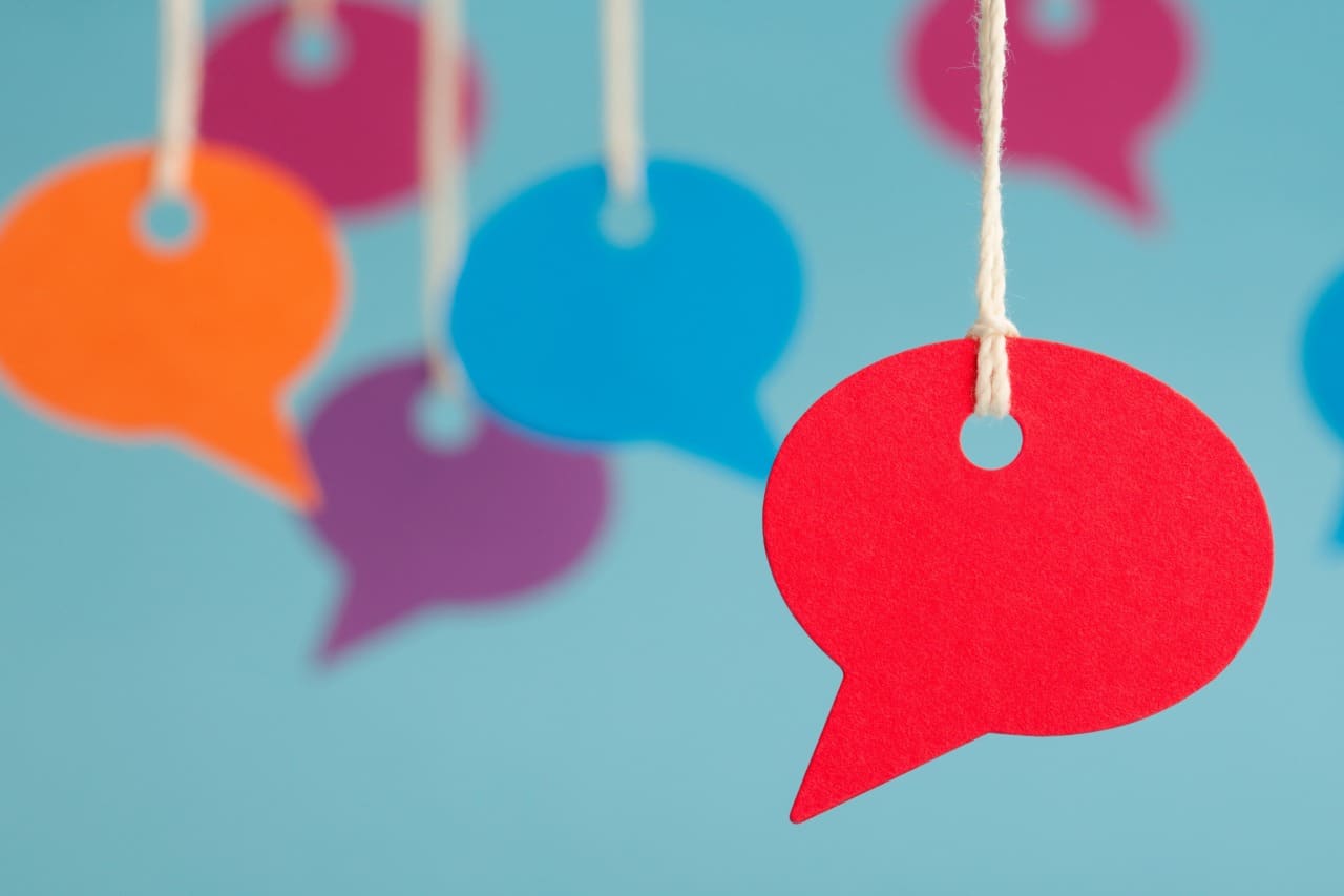Colourful paper speech bubbles hang from strings against a blue background, representing conversation or communication.